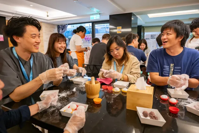 Participants wearing gloves shape mochi at tables during a hands-on food workshop