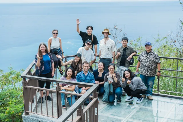 Group of about thirteen people posing and smiling on an outdoor viewing deck overlooking the ocean