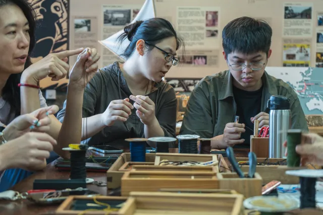 Participants focused on handcraft jewelry-making at a workshop table covered with tools and materials