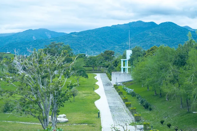 Winding path through a lush green park with mountains and cloudy sky in the background