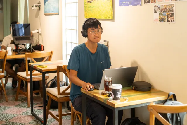 Young person with headphones working on a laptop at a cafe table