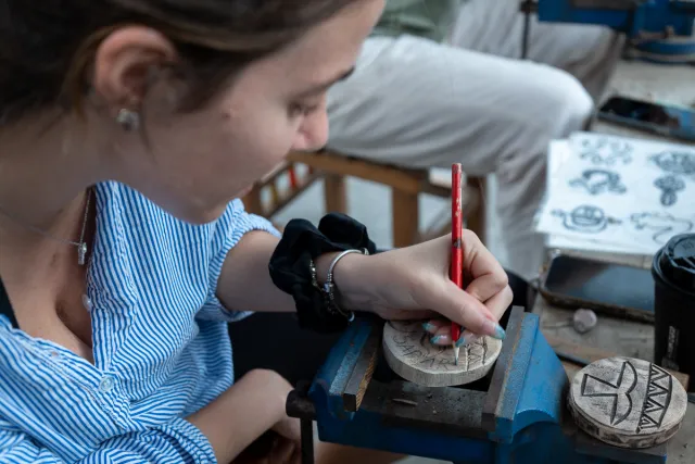 A woman carefully engraves a design onto a small stone disk at a craft workshop