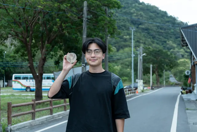 Young man smiling and holding up a small handcrafted disc on a rural road