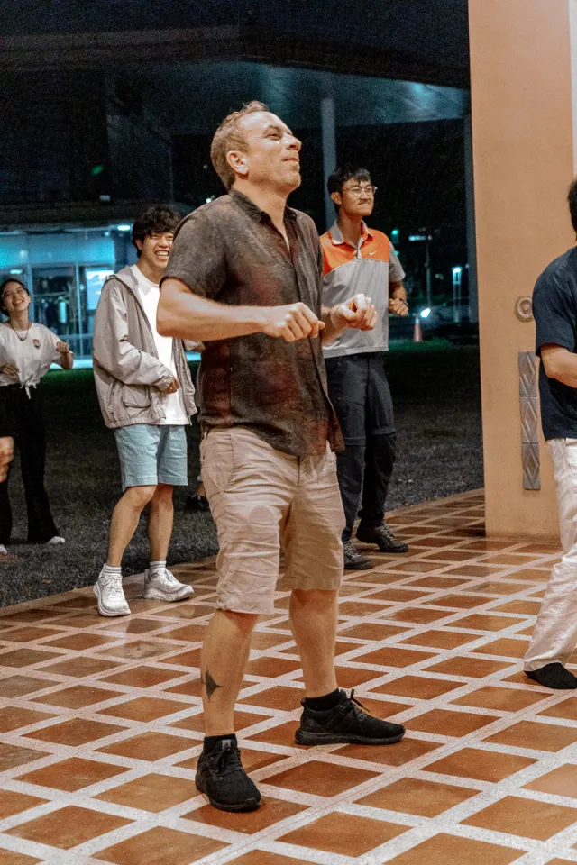 a man dances outdoors at night while smiling onlookers watch