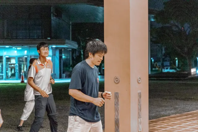 Two young men walking outdoors at night near an illuminated building colonnade