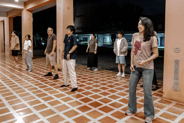 A group of people stand in a row practicing dance moves in an open-air covered space at night