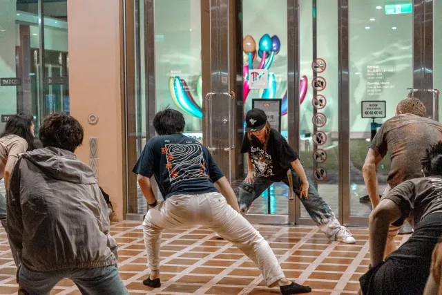 Several dancers in wide stances face off in an indoor hip-hop battle at night