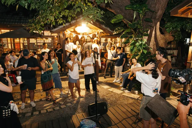 Crowd gathers around a performer with a microphone in a warmly lit outdoor courtyard at night