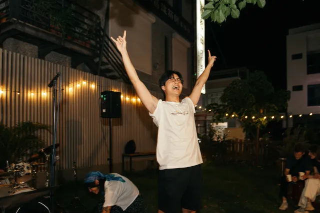 A young man raises both arms in celebration at an outdoor night jazz event