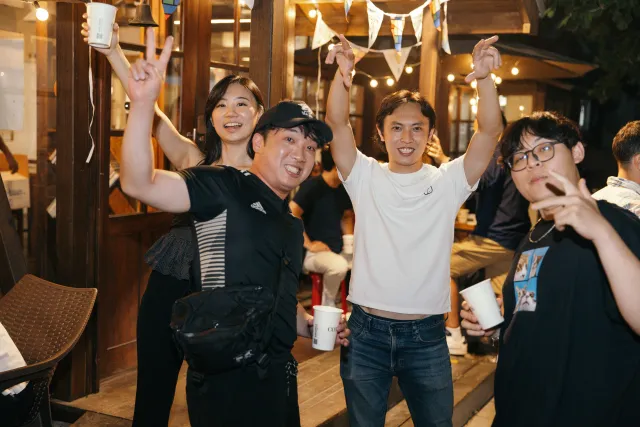 Four friends cheering with drinks raised at an outdoor evening gathering