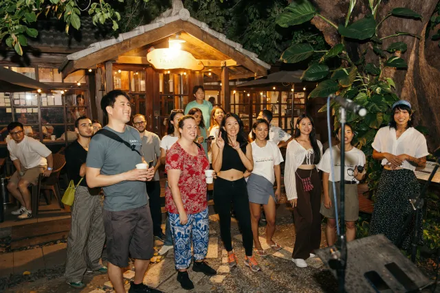 A crowd of guests smiling and watching a performance in a warmly lit outdoor garden venue at night