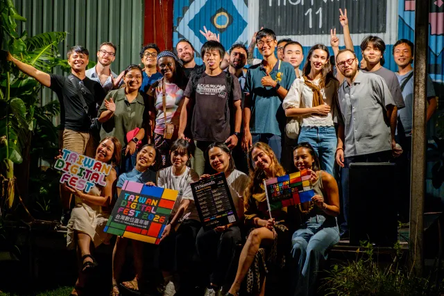 A diverse group of participants poses cheerfully outdoors at night holding Taiwan Digital Fest 2026 programs