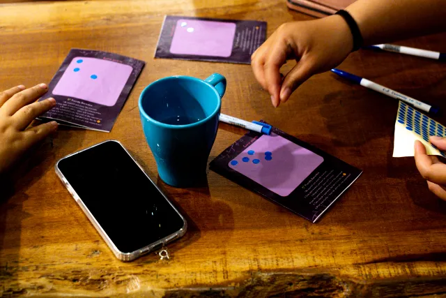 Participants arrange purple activity cards on a wooden table with a blue mug and a marker