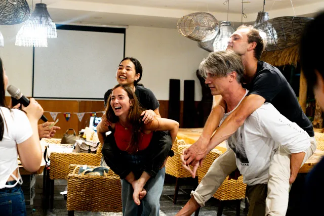 Two pairs of participants laugh during a piggyback-ride game at an indoor event