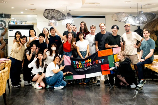 A large group of smiling participants poses indoors holding a Taiwan Digital Fest banner