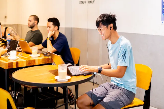 smiling man with earphones works on laptop at a cafe table
