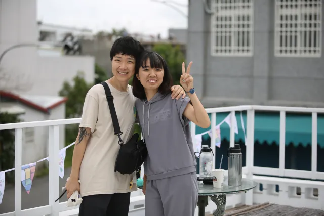 Two smiling women pose together on a rooftop terrace, one flashing a peace sign