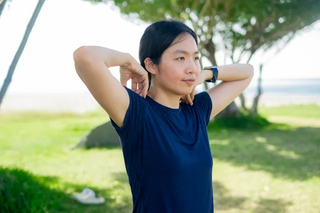 Woman in navy shirt stretching arms behind her head outdoors near the shore