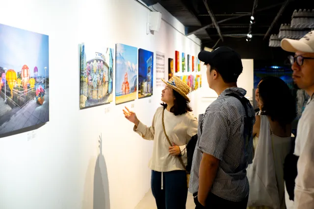 A guide gestures toward colorful photo prints on a gallery wall while visitors look on