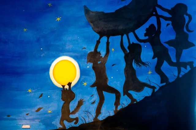 dark silhouettes of figures dancing and lifting a crescent moon under a starry blue night sky mural