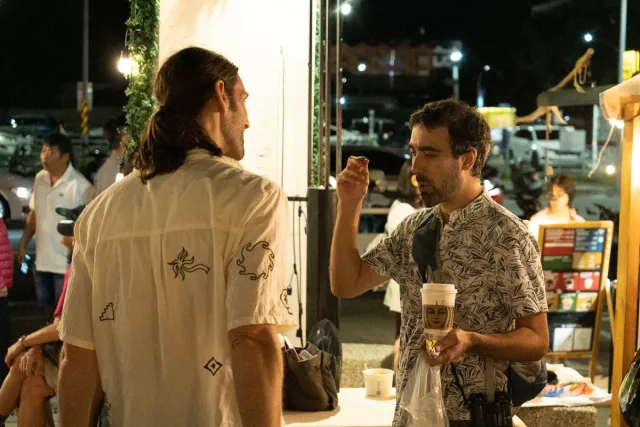 Two men chat and snack at an outdoor night market stall