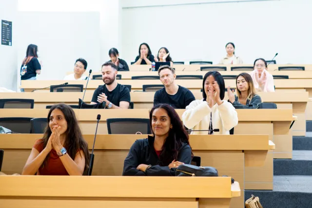 Diverse audience members smile and applaud during an indoor lecture session