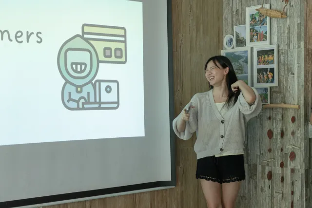 A smiling woman presents to an audience beside a projected slide showing a hacker icon