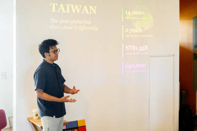 A speaker gestures while presenting Taiwan statistics on a projected slide indoors