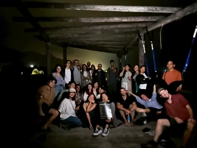 A large group of people posing together indoors at night under a rustic open-air structure