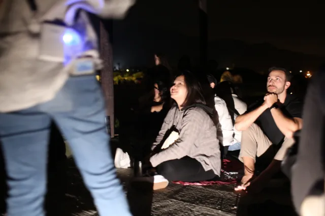 Participants sit outdoors at night gazing upward with wonder during a stargazing event