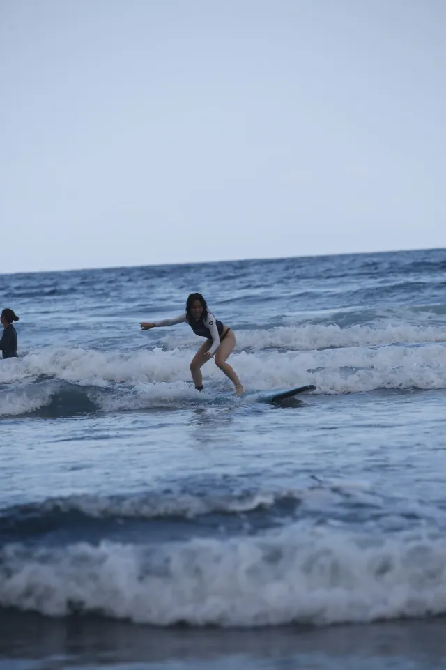 A woman rides a wave on a surfboard in the ocean, arms outstretched for balance