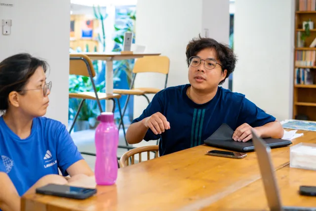 Two participants in conversation at a wooden table during an indoor workshop session