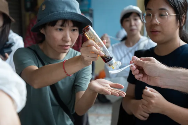 a participant pours sauce from a bottle onto a spoon held by another person