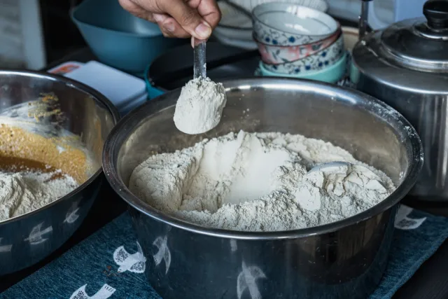 A hand scoops white flour from a large metal mixing bowl during food preparation