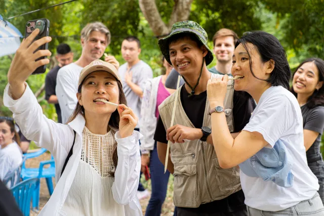 Smiling participants take a selfie and chew on sticks outdoors during a forest activity