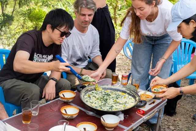 participants gathered around a large pan of cooked greens, serving themselves outdoors