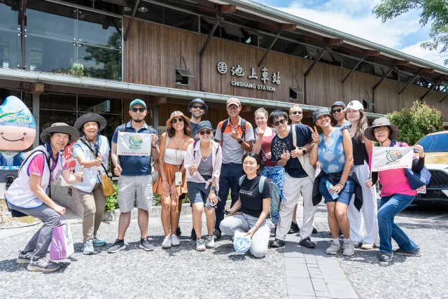 A tour group poses cheerfully in front of Chishang Station on a sunny day