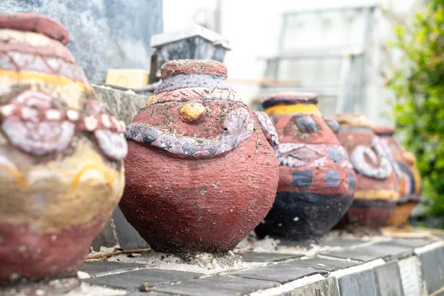 Weathered decorative clay pots with painted indigenous motifs lined up outdoors