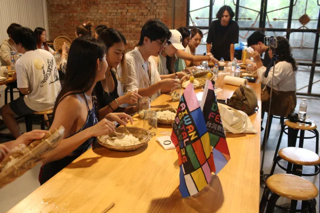 participants hand-mixing rice at a long wooden table during a brewing workshop