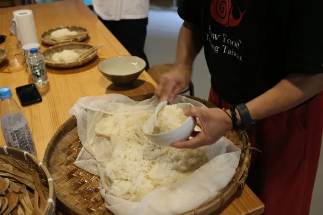 participant scoops cooked rice into a large bamboo tray during a fermentation workshop