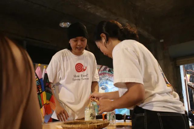 Two participants in white T-shirts work together at a table during a brewing workshop