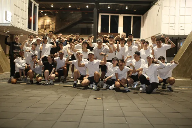Large group of participants in white shirts posing together at night, flexing arms