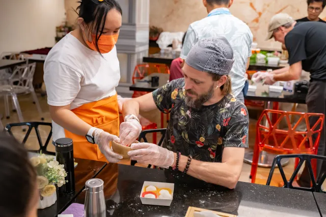 Instructor guides a participant shaping a pastry during an indoor hands-on workshop