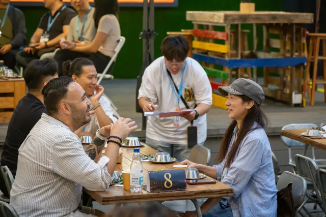 Two participants chat animatedly at a numbered table in a warmly lit indoor event space