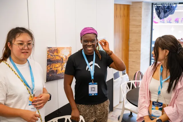 Three participants wearing lanyards smiling and chatting indoors at an event venue