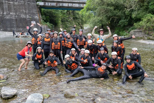 Large group in wetsuits and life jackets posing cheerfully in a shallow river