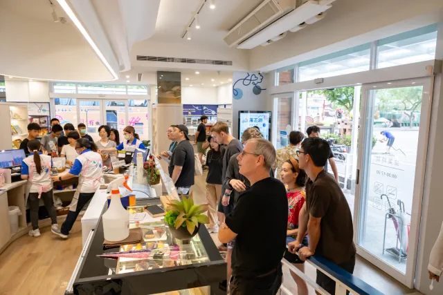 Visitors browse display counters inside a bright retail shop while staff assist customers