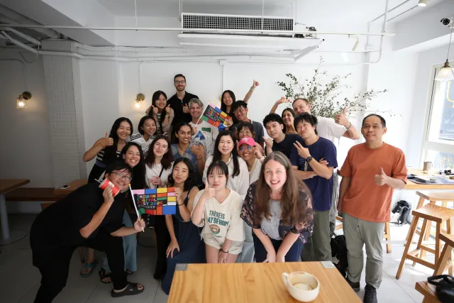 A large group of smiling participants poses together inside a bright cafe
