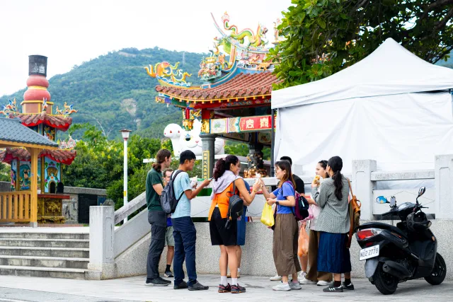 Small group of people chatting and eating outdoors near a traditional Taiwanese temple