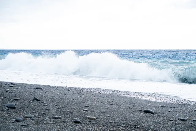 Waves crashing onto a dark pebble beach under an overcast sky